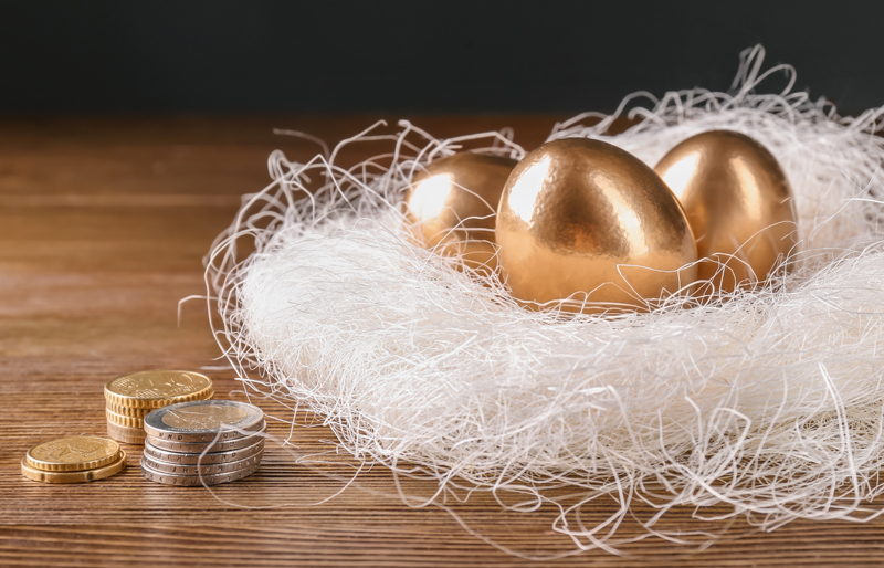 Trois œufs en métal précieux sont déposés dans un nid de ficelle blanche, à coté de petites piles de pièces de monnaie.