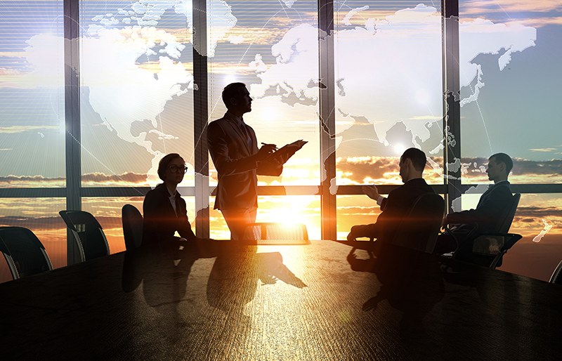 Des professionnels se consultent dans une salle de réunion avec vue sur un coucher de soleil et superposée à l’image, une carte du monde.