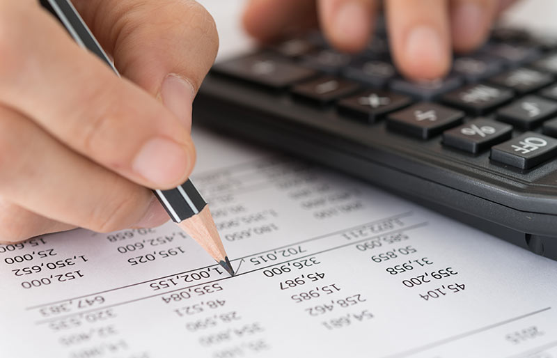 A close- up of a hand checking a financial statement using calculator and pencil.