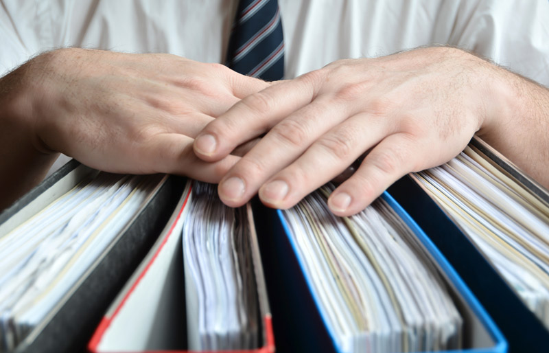 A close-up image of a males hands holding numerous binders. 
