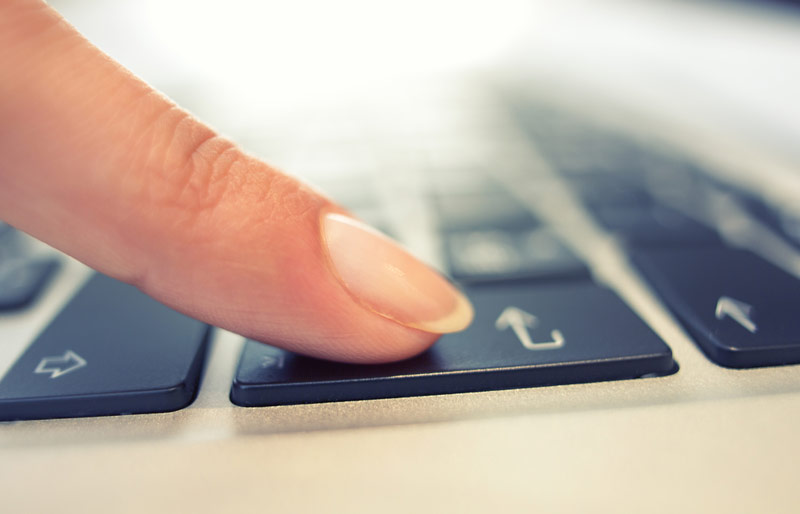 Close up of finger hitting "enter" key on laptop keyboard