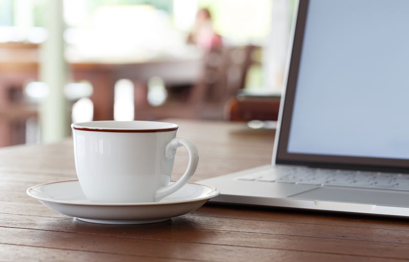 A close-up image of a laptop and a coffee cup sitting on a desk. 