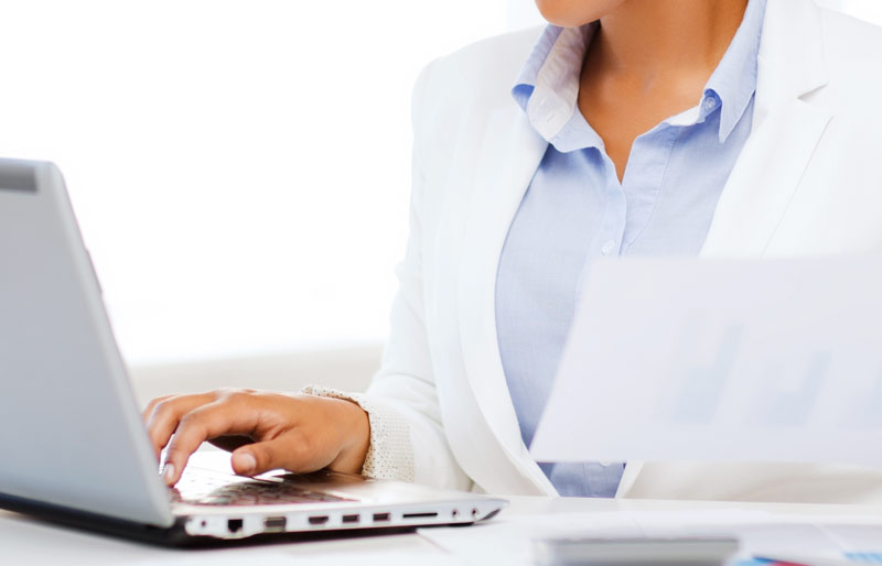 A businesswoman looking at her laptop while holding a piece of paper. 