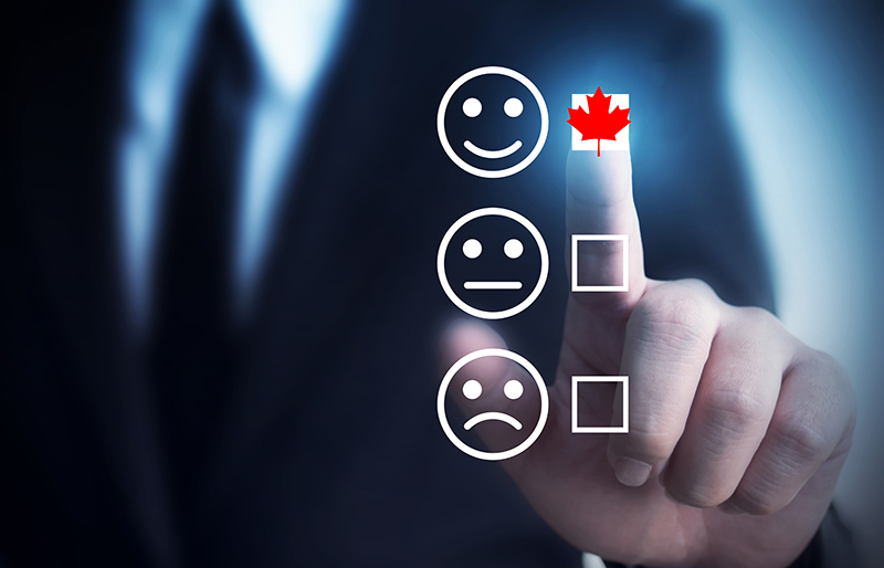 The finger of a business person selecting a box with a Canadian red maple leaf beside a smiley-face icon above a neutral-face icon and sad-face icon with boxes not selected