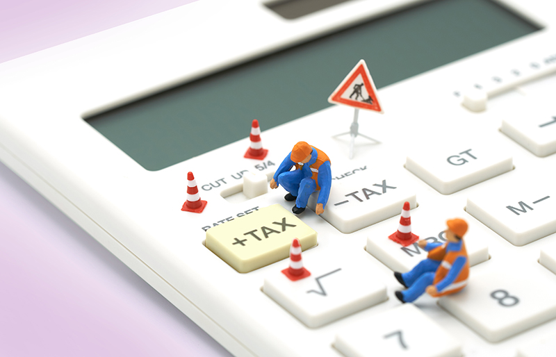 A real Calculator with miniature workers and orange road cones around them, looking at the TAX button on the calculator