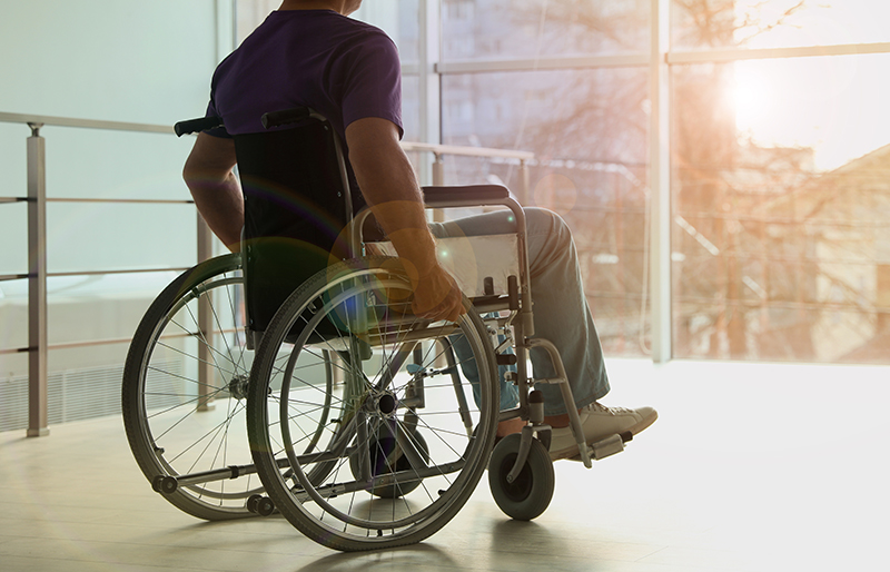 Person sitting in a wheelchair, looking out a large window to the outside