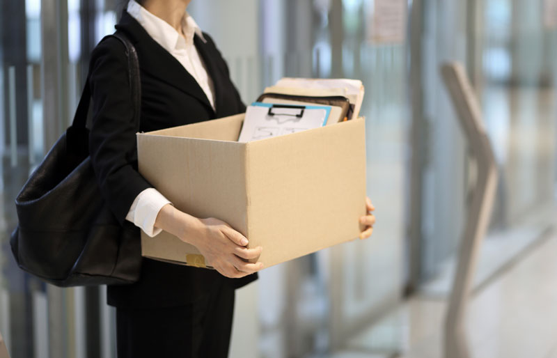 Businesswoman leaving office with a box of personal items.