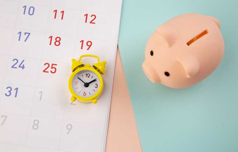 Piggy bank and alarm clock with calendar on colorful background