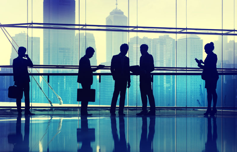 Silhouettes of five business people standing in front of downtown office windows.
