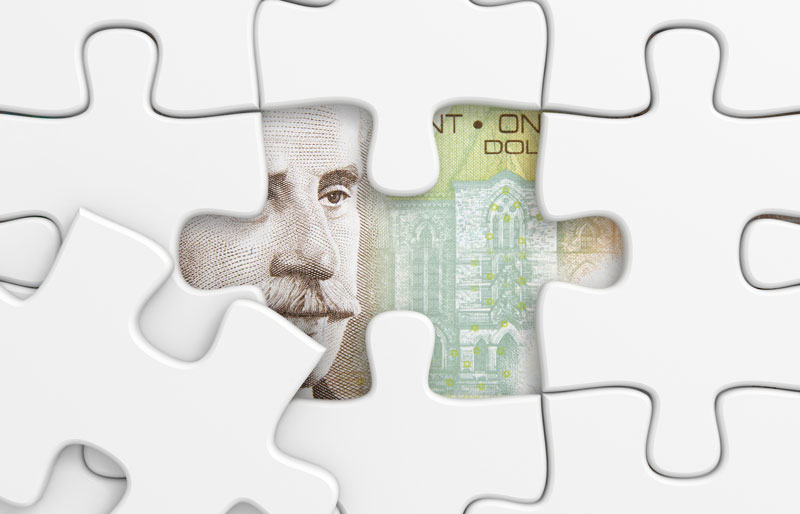 White jigsaw puzzle with one piece missing, revealing a Canadian $100 bill beneath.
