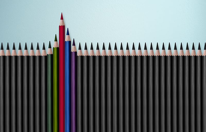 Rangée de crayons noirs de taille identique au milieu de laquelle se distinguent cinq plus grands crayons de couleurs diverses.